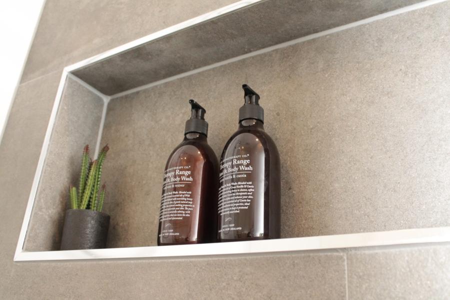 Recessed bathroom niche with two amber pump bottles and a small potted plant