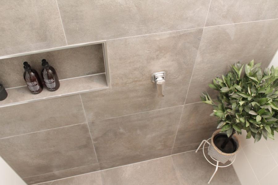 Grey tiled shower wall with recessed niche, fittings and potted plant