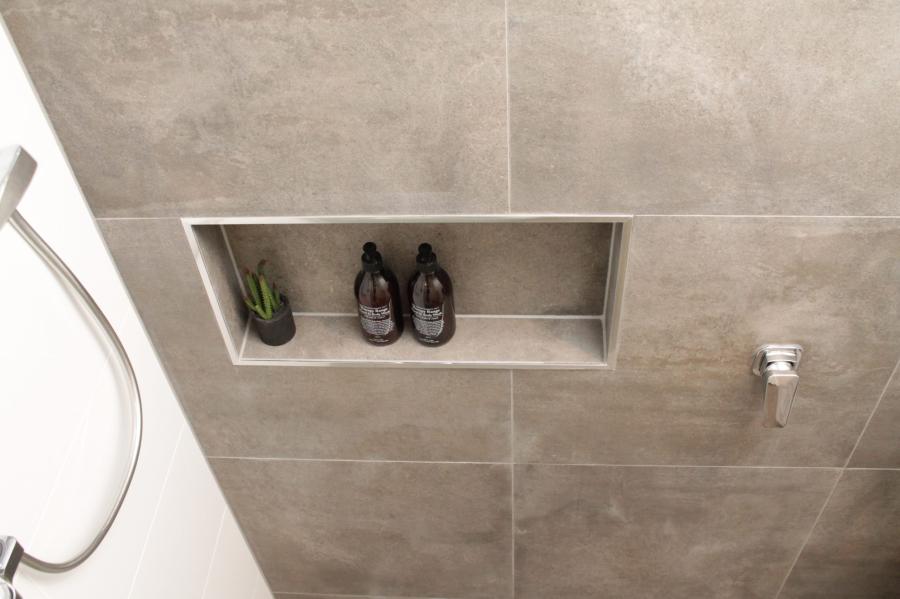 Recessed shower niche in a grey tiled bathroom wall with toiletries