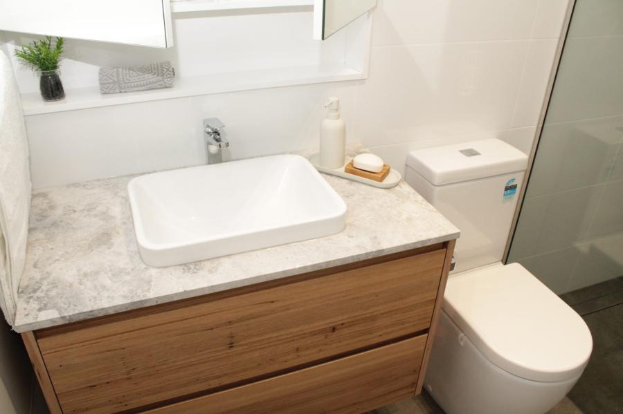 Modern bathroom vanity with vessel basin, timber drawers and toilet beside a glass shower