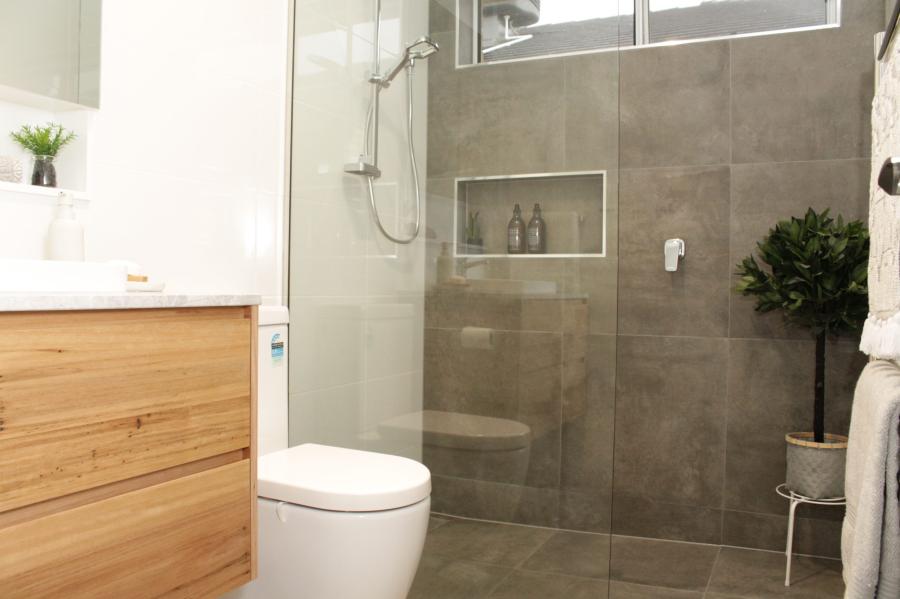 Modern bathroom with timber vanity, toilet and grey tiled walk-in shower