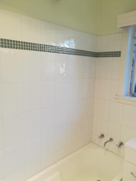 Older bathroom with white wall tiles, mosaic border and bathtub before renovation