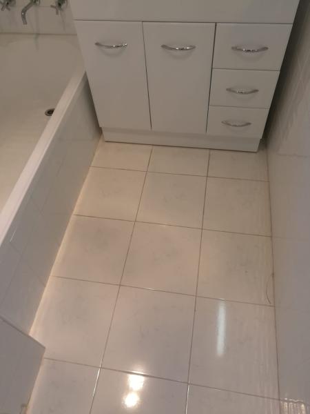 White tiled bathroom floor beside bathtub and vanity with visible grout discolouration