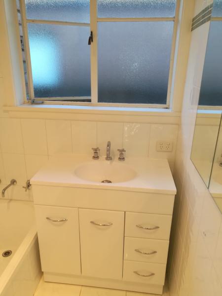 White bathroom vanity with inset basin beneath a frosted window and mirrored wall
