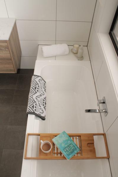 Modern white bathtub with timber caddy in a minimalist tiled bathroom