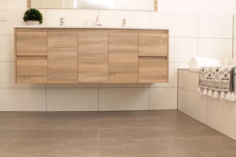 Floating timber vanity in a modern tiled bathroom with white basin and built-in bath