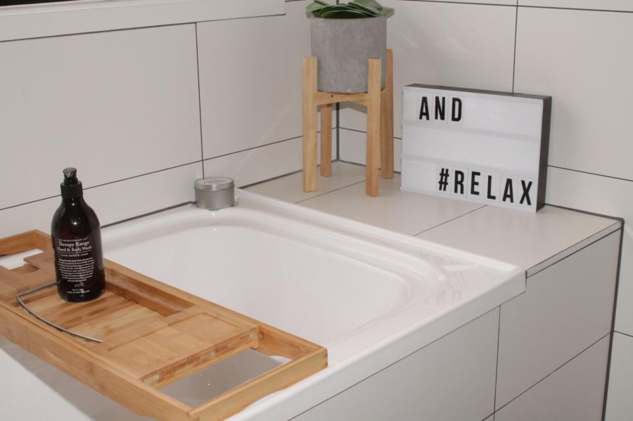 Modern white bathtub with timber bath tray, tiled surround and relax sign