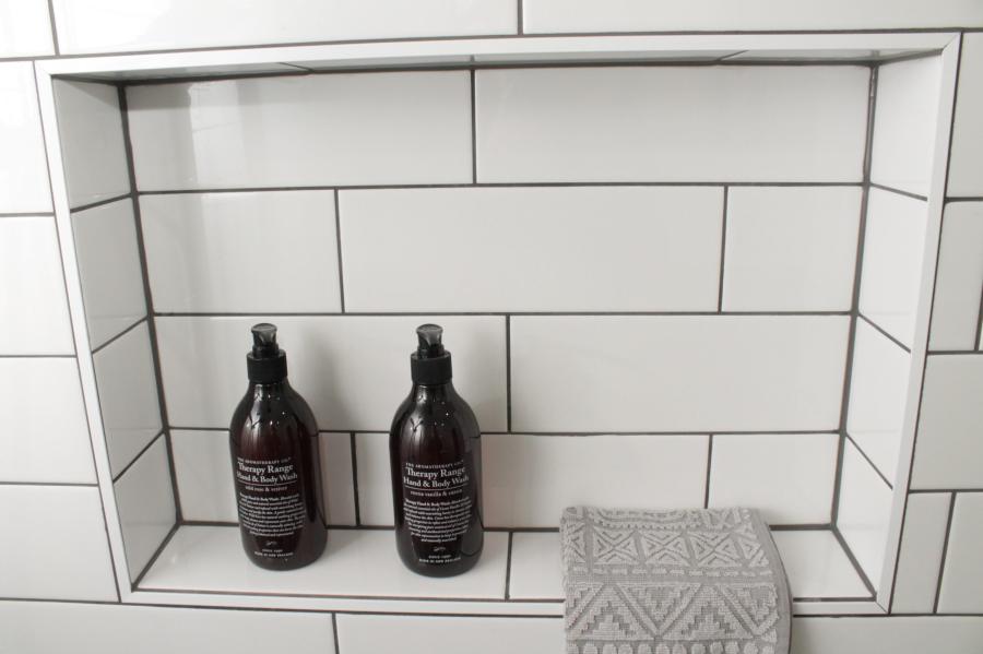 Recessed shower niche with white subway tiles, two dark bottles and folded grey towel