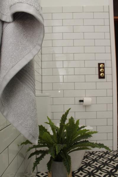 Grey towel hanging beside white subway tiles with a fern and patterned floor in a modern bathroom
