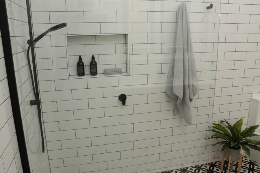 Walk-in shower with white subway tiles, recessed niche and matte black shower rail