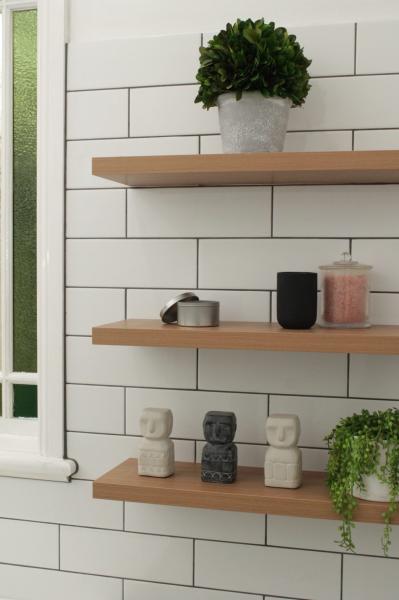 Floating timber shelves on a white tiled bathroom wall with plants and decorative accessories