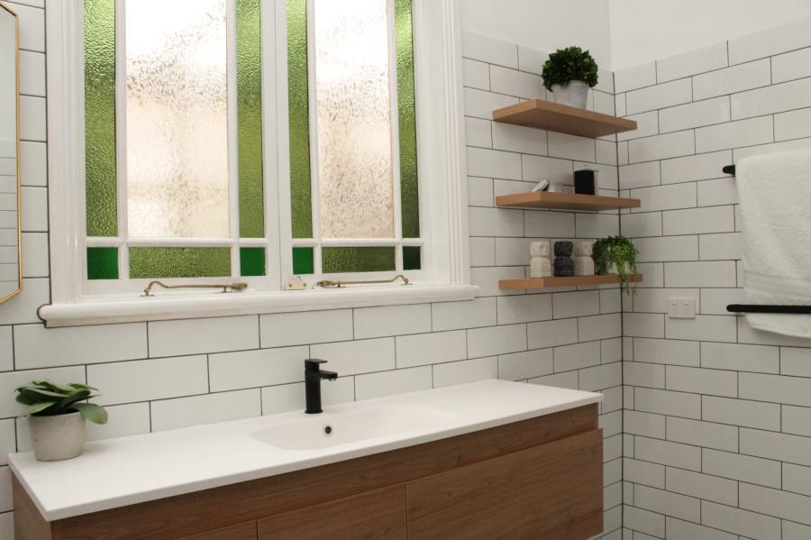 Modern bathroom vanity with white subway tiles, black tapware and frosted green window panels