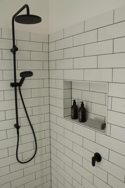 White tiled shower with black tapware and recessed niche