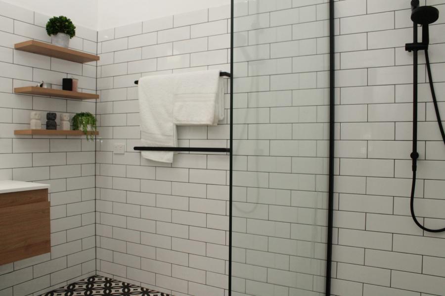 Modern white tiled shower with black fixtures, glass screen and timber vanity