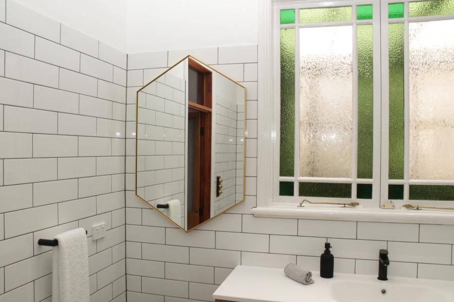 Bright bathroom vanity with white subway tiles, mirror cabinet and frosted stained glass window