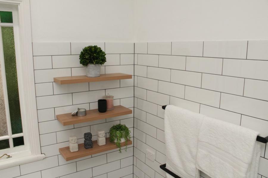 White tiled bathroom corner with timber floating shelves and folded white towels