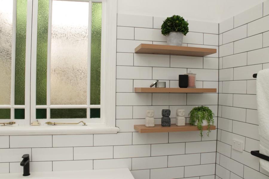White tiled bathroom with frosted window, timber shelves and black tapware