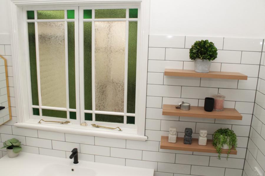 White tiled bathroom wall with frosted window, timber shelves and black tapware