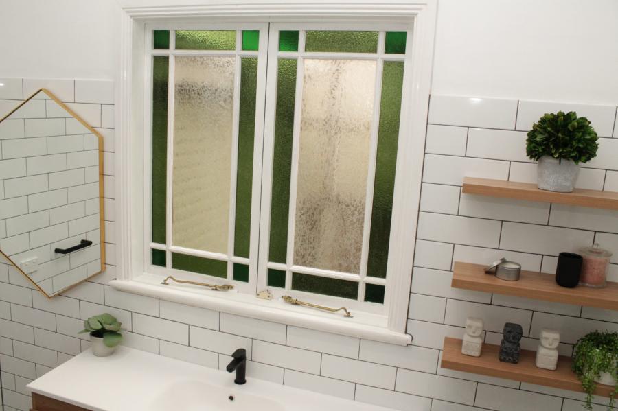Bright bathroom with white subway tiles, frosted window, black tapware and timber shelving