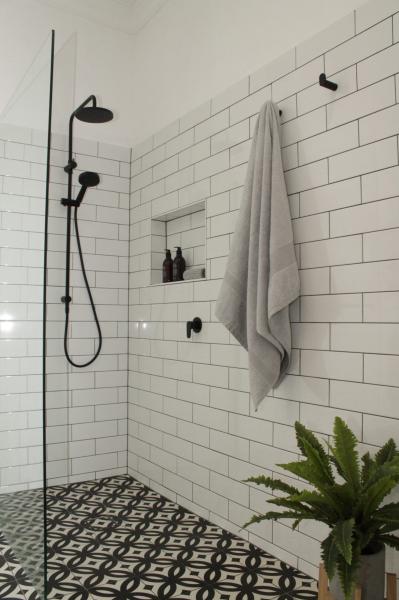 Walk-in shower with white subway tiles, black tapware and patterned floor tiles