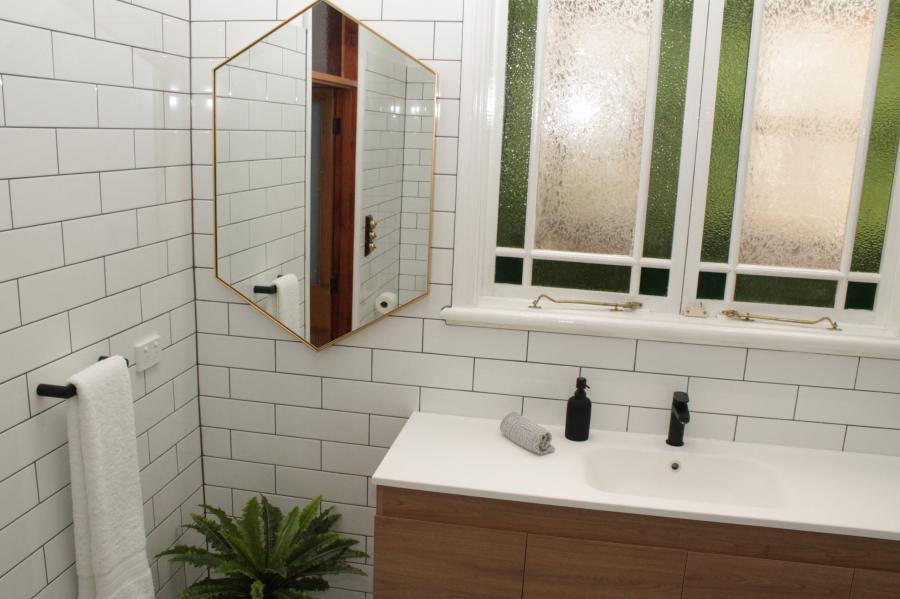 White tiled bathroom vanity with mirrored cabinet beneath frosted window