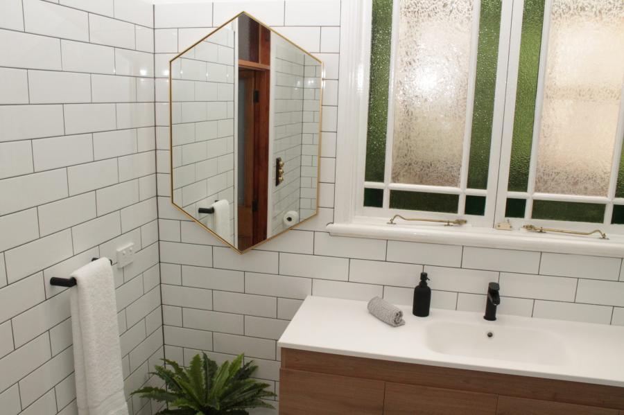 Modern bathroom vanity with white subway tiles, hexagonal mirror and frosted window