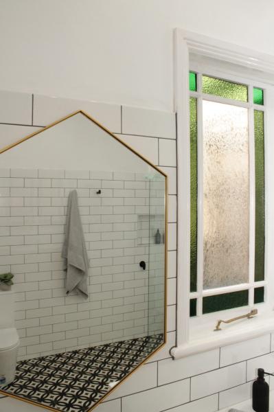 Bathroom shower with white subway tiles, patterned floor, brass trim and frosted window