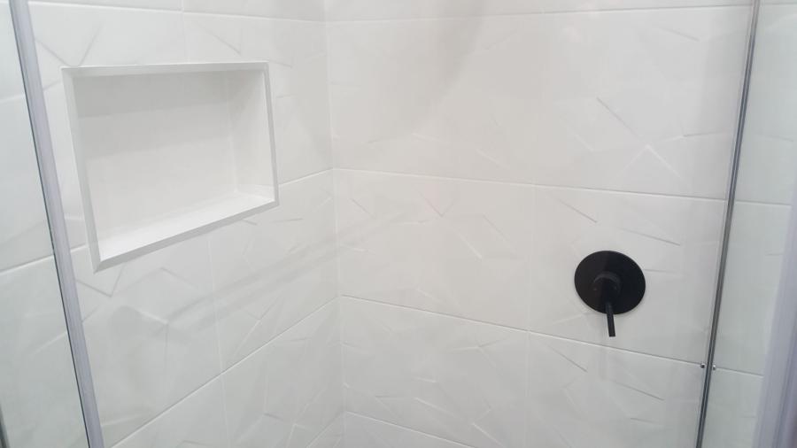 White tiled shower with recessed niche and matte black mixer behind glass screen