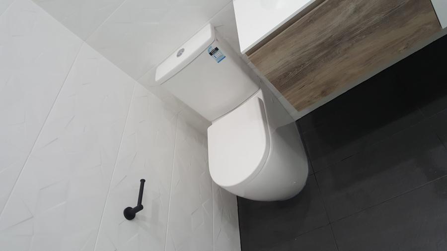 Modern white wall-faced toilet beside timber vanity on dark tiled bathroom floor