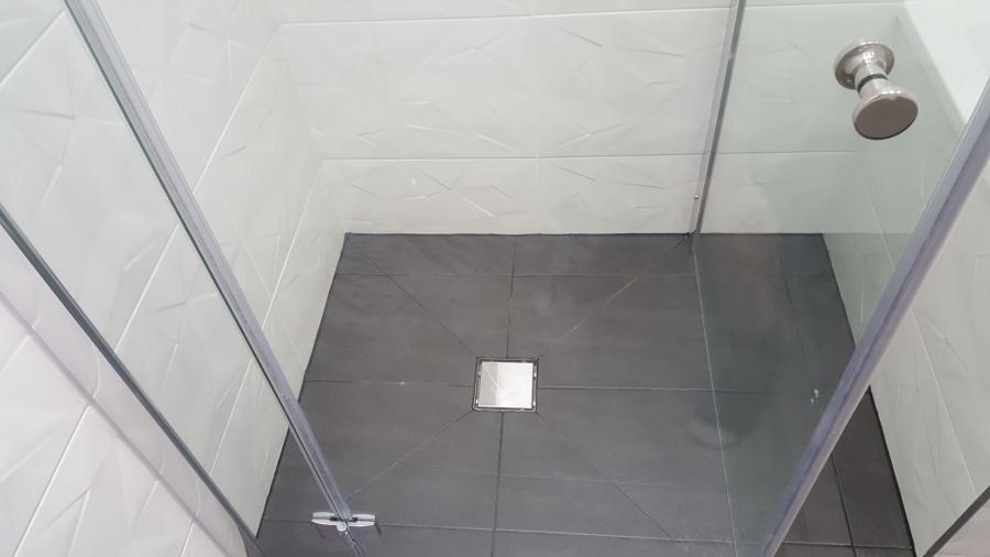 Walk-in tiled shower with grey floor tiles, square drain and frameless glass screen