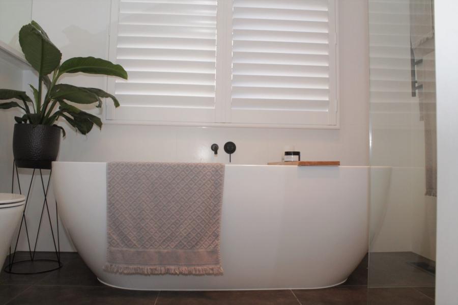 Freestanding white bathtub beneath plantation shutters in a modern bathroom