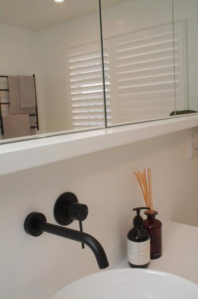 Matte black wall-mounted bathroom tap beside basin and accessories
