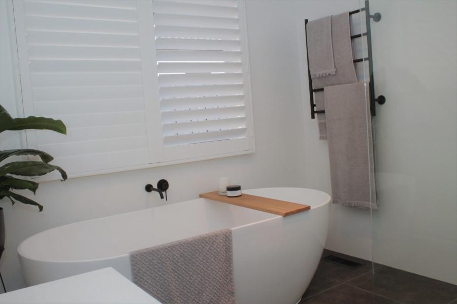 Modern white freestanding bath with timber caddy and towel rail in a bright minimalist bathroom