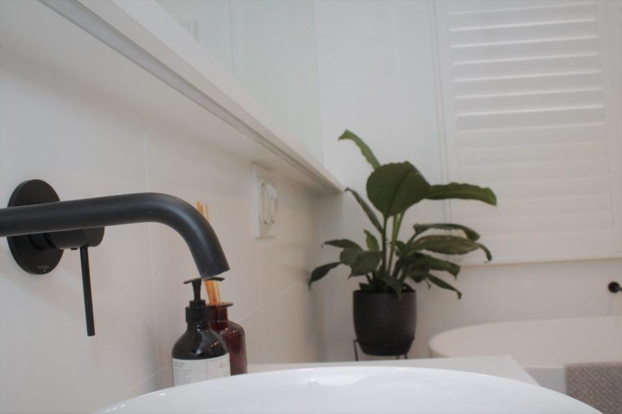 Matte black bathroom tap beside a basin, with a potted plant and white shutters in the background