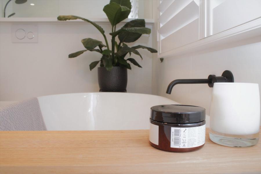 Bathroom styling detail with freestanding bath, timber bench, plant and matte black wall tapware