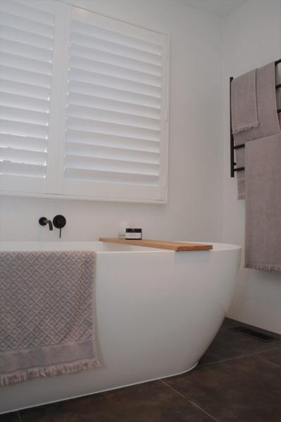 Freestanding white bath beneath plantation shutters in a modern bathroom