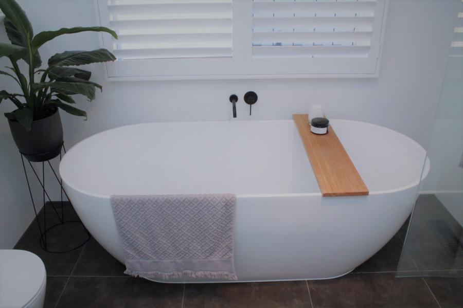 Freestanding white bathtub with timber bath caddy in a modern tiled bathroom