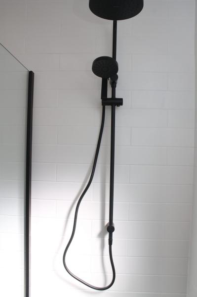 Matte black shower rail and handheld shower on white tiled bathroom wall
