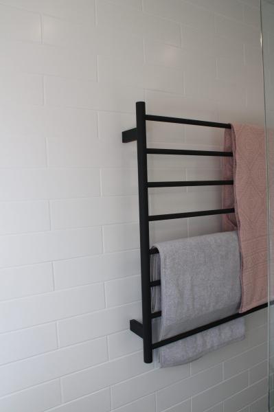 Black heated towel rail with white and pink towels on a white tiled bathroom wall