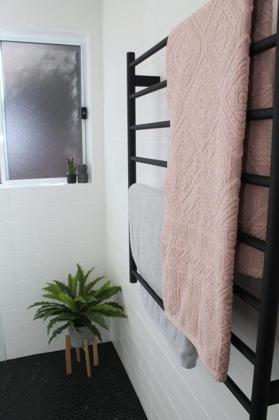 Black heated towel rail with pink towel beside white bath and frosted bathroom window