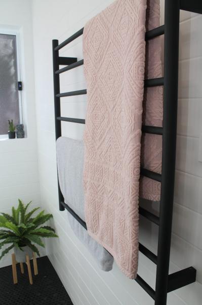 Black heated towel rail with pink towel in a modern white tiled bathroom