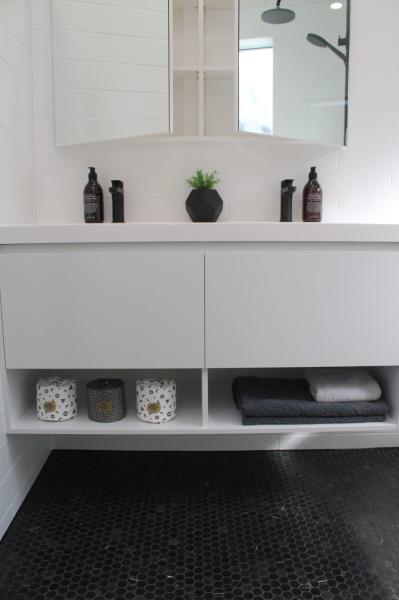 Floating white bathroom vanity with open shelf storage beneath a mirrored cabinet