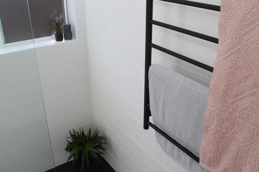 Modern white tiled bathroom with black towel rail and folded towels