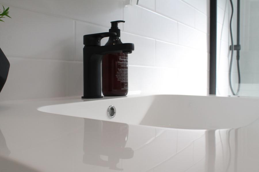 White bathroom basin with black soap dispenser beside a glass shower screen