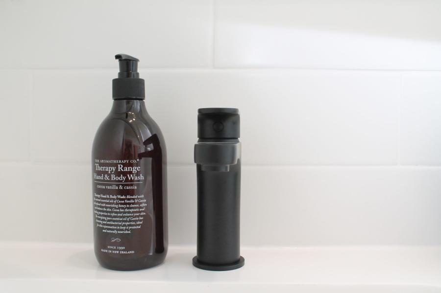 Amber hand wash bottle and black soap dispenser on a white tiled bathroom ledge