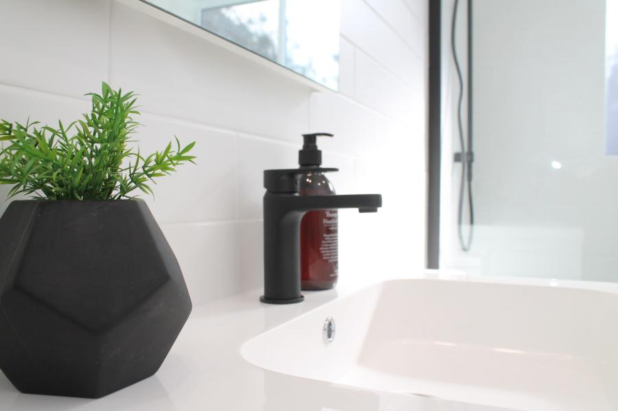 Matte black basin tap beside a white sink and potted plant in a modern bathroom