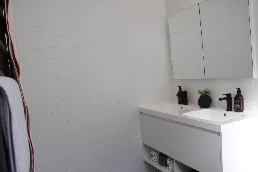 White bathroom vanity with mirror cabinet, black tapware and white tiled wall