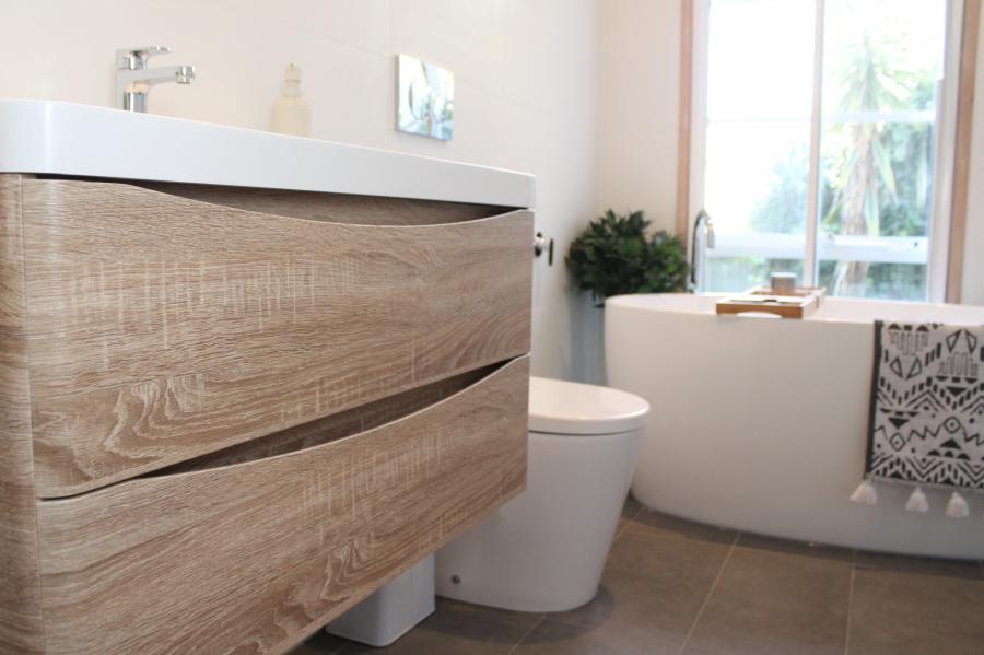 Timber floating vanity beside toilet and bath in a modern bathroom