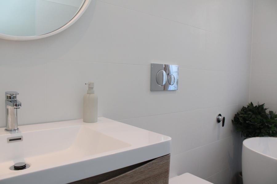 Modern white bathroom vanity with basin, chrome tap, wall-hung toilet and round mirror