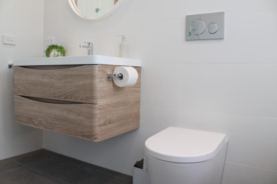 Wall-hung timber vanity and toilet in a modern white bathroom